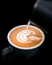 Close-up of a barista pouring latte art in a stylish ceramic cup on a wooden table.