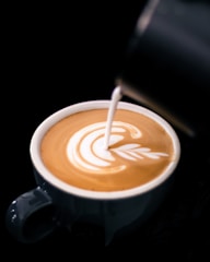 Close-up of a barista pouring latte art into a ceramic cup at a sleek espresso bar.