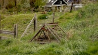 Traditional agricultural tools resting on a wooden fence in a village landscape.