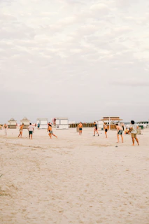 A close-up of a beach soccer match with players diving for the ball on golden sand.