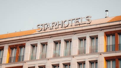 A multi-story building with a sign reading 'STARHOTELS' on the rooftop. The facade features a series of evenly spaced windows with decorative railings. The building exhibits a modern architectural design with clean lines and a neutral color palette.
