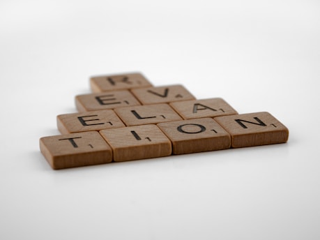 Wooden letter tiles arranged to spell 'Revelation' in a staggered formation on a plain white background.