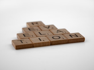 Wooden letter tiles arranged to spell 'Revelation' in a staggered formation on a plain white background.
