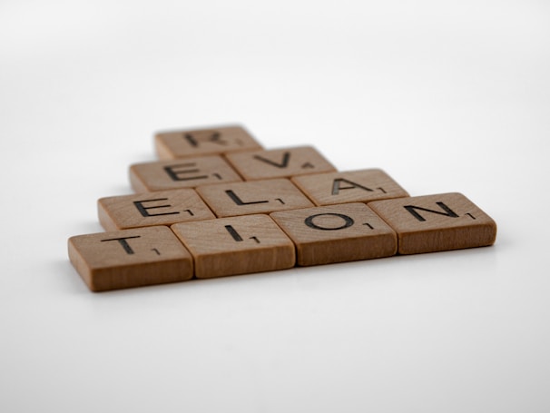 Wooden letter tiles arranged to spell 'Revelation' in a staggered formation on a plain white background.