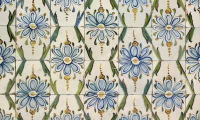 A pattern of ceramic tiles featuring blue and yellow floral designs with green accents. The tiles are arranged in a repeating motif, showcasing intricate flower shapes and leaf-like forms.