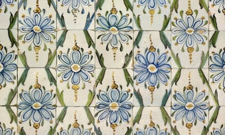 A pattern of ceramic tiles featuring blue and yellow floral designs with green accents. The tiles are arranged in a repeating motif, showcasing intricate flower shapes and leaf-like forms.