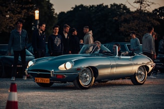 A vintage car gathering at sunset with smiling people chatting around classic vehicles.