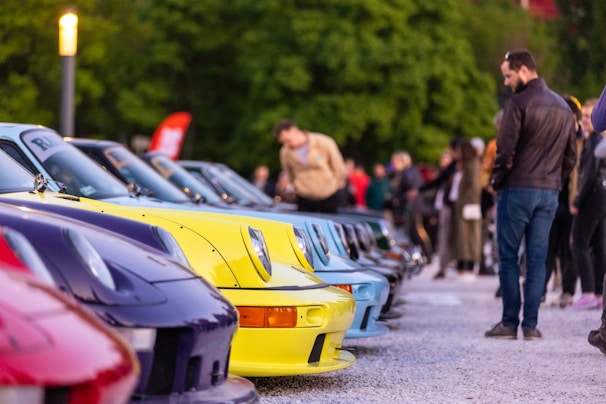 A row of gleaming classic cars lined up on a green lawn, with enthusiastic visitors admiring the vehicles during a lively car show.