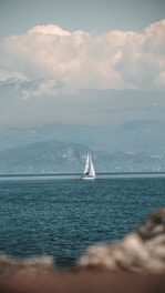 A sailboat gliding on calm waters with mountainous coastline in the background.