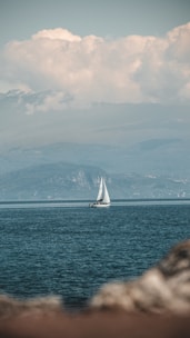 A sailboat gliding on calm waters with mountainous coastline in the background.