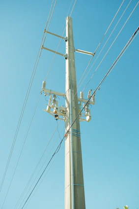 A close-up of a sturdy steel pole standing tall against a clear blue sky, with electric lines stretching into the distance.