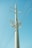 A tall electricity pole stands against a clear blue sky, with multiple lines of cables stretching outwards. The pole is equipped with insulators and other electrical components.