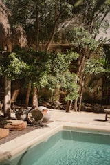 Swimming pool area with jacuzzi and shaded outdoor seating surrounded by trees.