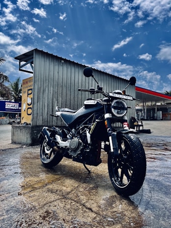 The electric motorcycle parked beside a modern building, droplets of rain highlighting its smooth aerodynamic design.