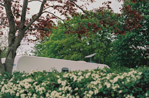 A bright, modern static caravan with a wooden deck surrounded by lush greenery at Stanhope Burn Park.