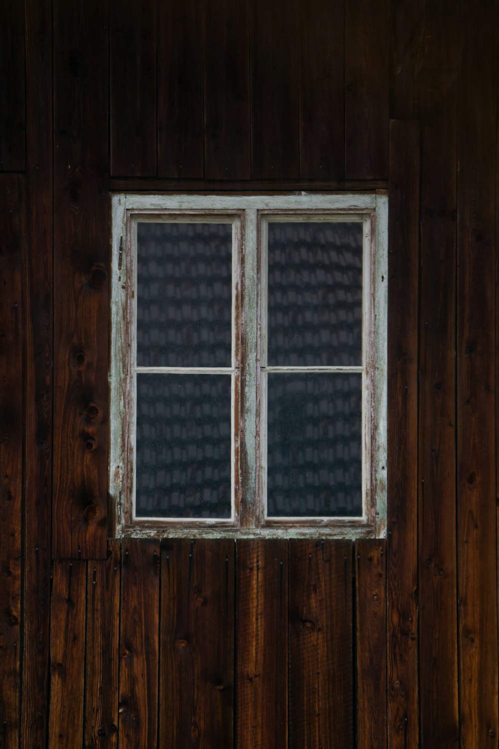 a window on a wooden wall with a bench in front of it