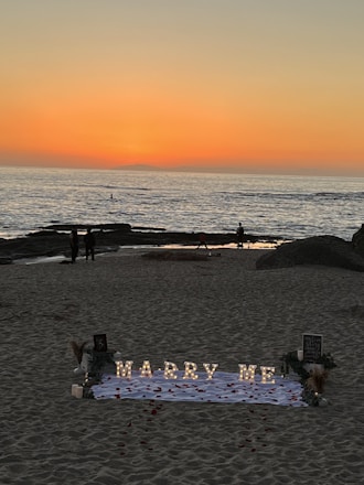 A romantic beach sunset setup with elegant floral arrangements and a couple sharing a joyful moment.