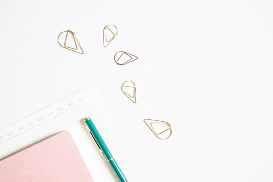 Unbranded pink notebook, cream paper, pen and paper clips on a white desk
