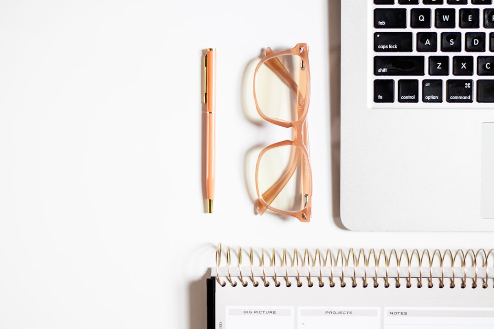 a desk with a laptop, glasses, and a notepad