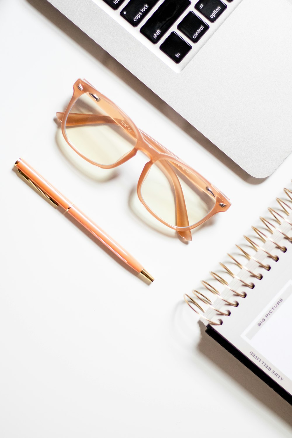 ein Notizbuch, einen Stift, eine Brille und einen Laptop auf einem Schreibtisch