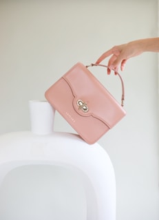 a woman holding a pink purse over a white vase