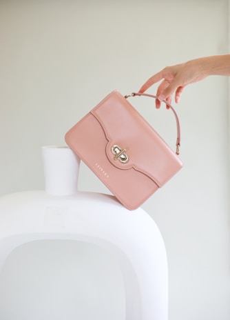 a woman holding a pink purse over a white vase