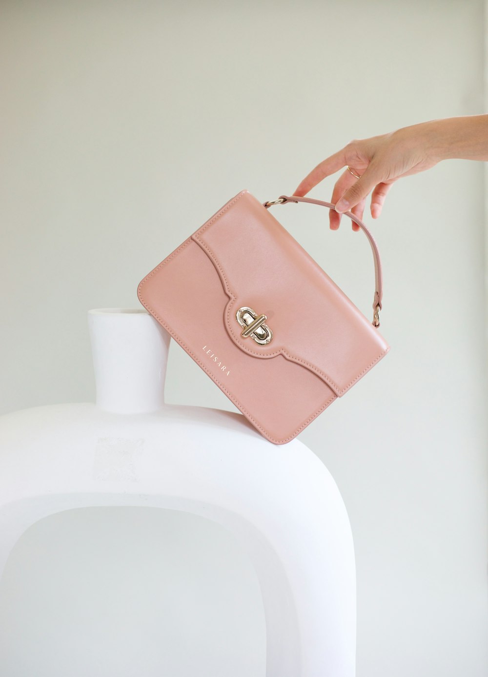 a woman holding a pink purse over a white vase