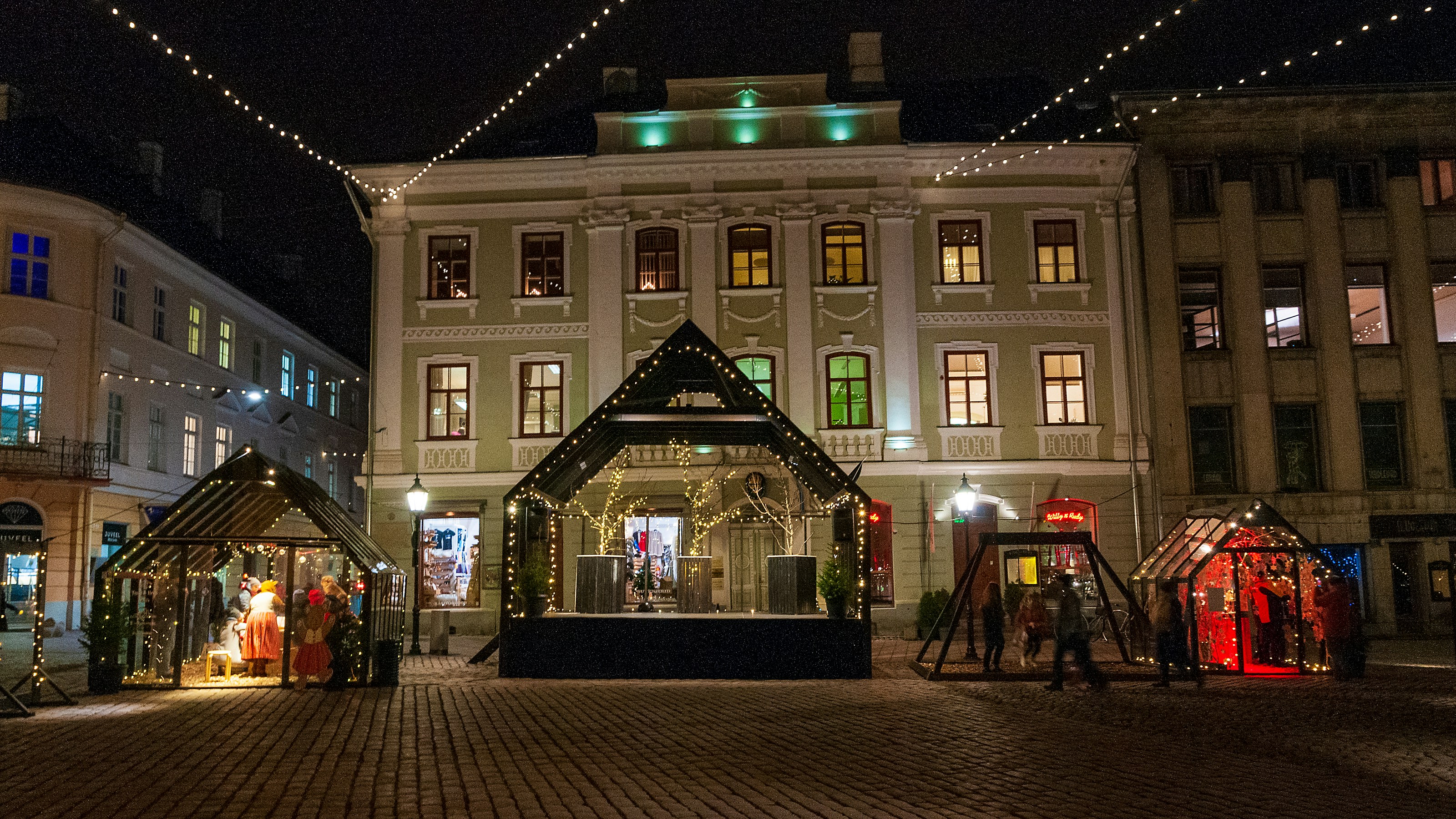 Alsace Christmas market at night, illuminated half-timbered buildings, snow, festive lights, warm glow