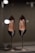 A pair of elegant black leather high-heeled shoes displayed on metal stands. The shoes appear sleek and sophisticated, with a glossy finish. Reflective lights above enhance their shine and highlight the brand name inside the shoes.