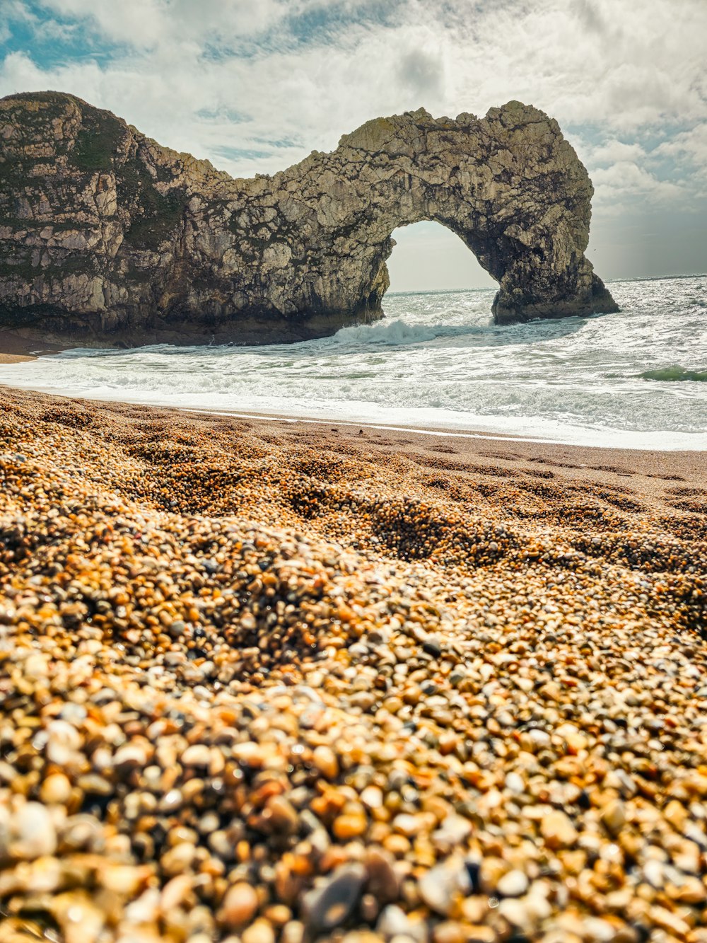 a rocky beach with a rock arch in the background