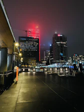 A misty cityscape at night with gold and deep red lights reflecting off wet streets.