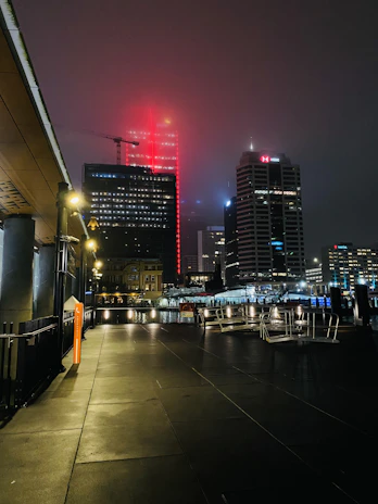 A misty cityscape at night with gold and deep red lights reflecting off wet streets.