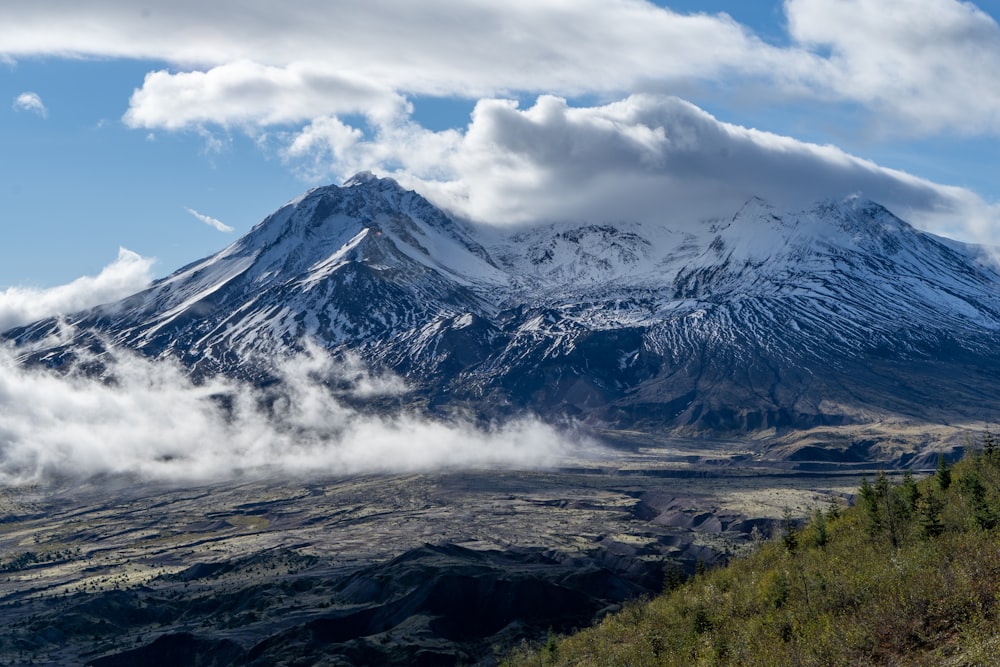 a mountain covered in snow and clouds on a sunny day