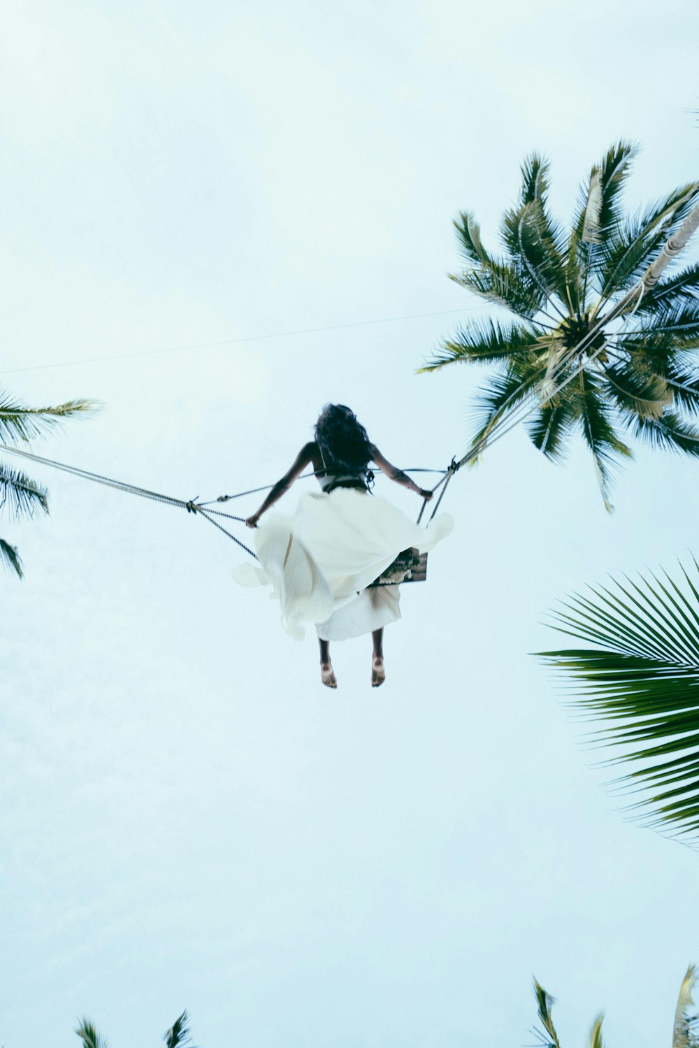uma mulher em um vestido branco em uma corda entre duas palmeiras