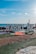Large white letters spelling 'MARRY ME' are set up on a grassy outdoor area overlooking the sea. A red carpet leads up to the letters, with candles arranged along the sides. The sky is clear and blue, contributing to a romantic setting.