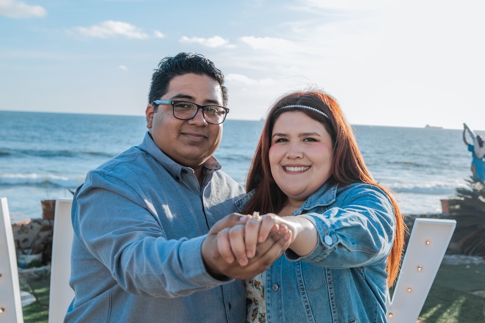 a man and a woman standing next to each other near the ocean