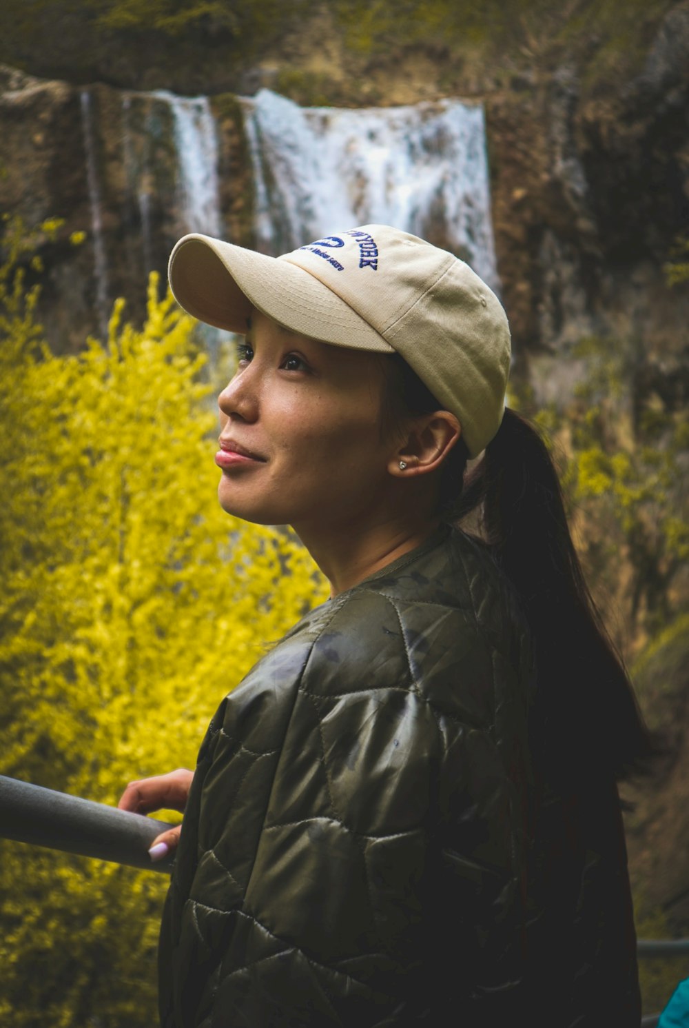 a woman wearing a hat standing in front of a waterfall