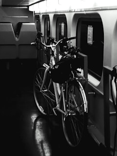 A bicycle is parked inside a train compartment next to a row of windows. The interior is dimly lit, giving a moody atmosphere. The reflection of the bicycle can be seen on the dark, glossy floor.