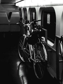 A bicycle is parked inside a train compartment next to a row of windows. The interior is dimly lit, giving a moody atmosphere. The reflection of the bicycle can be seen on the dark, glossy floor.