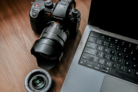 Close-up of a professional camera resting on a wooden desk next to a laptop.