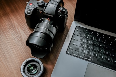 Compact cube camera sitting on a wooden desk beside a laptop.