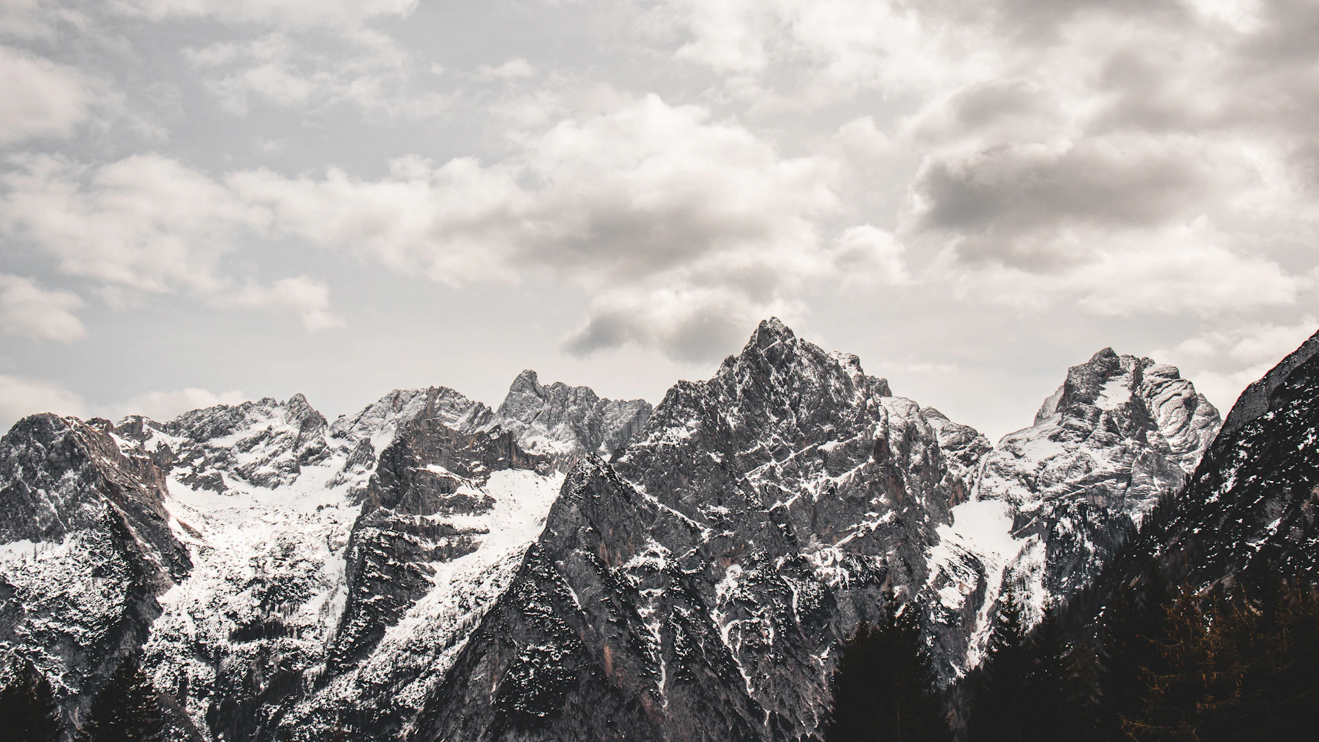a mountain range covered in snow under a cloudy sky
