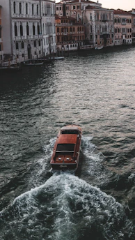 A turquoise-hued electric canal boat gliding smoothly along a serene canal at sunset