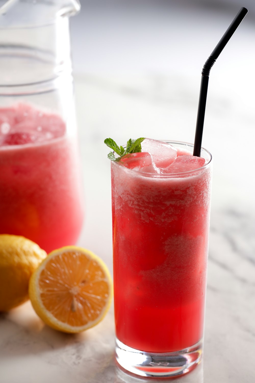 a glass of watermelon lemonade next to a pitcher of watermelon