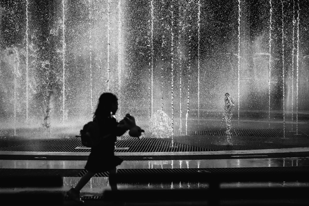 a woman walking past a water fountain in black and white