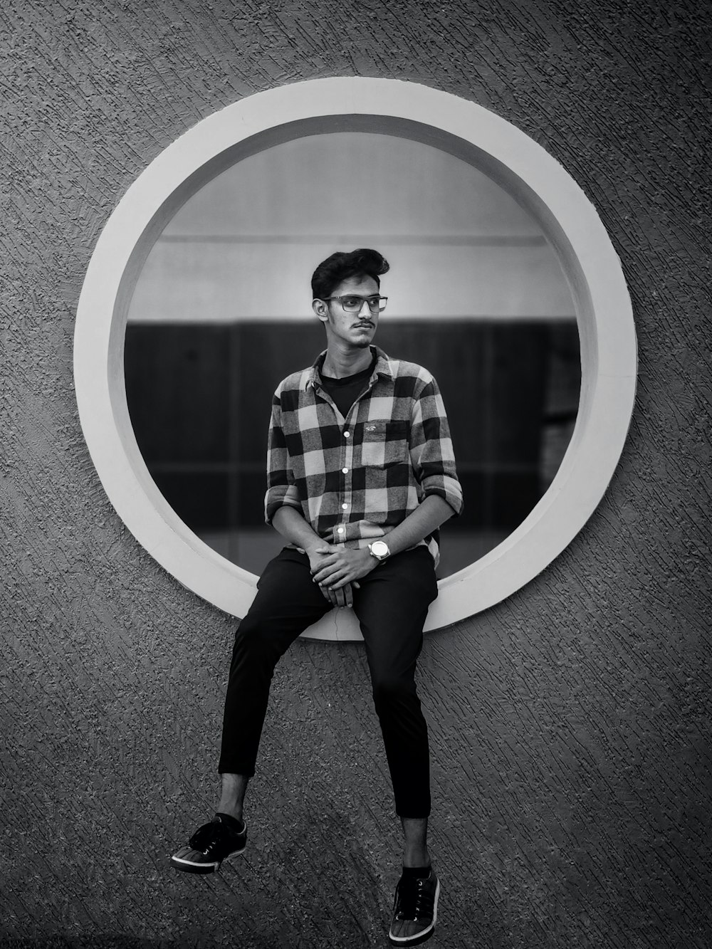 Un hombre está sentado en una pared con un espejo circular