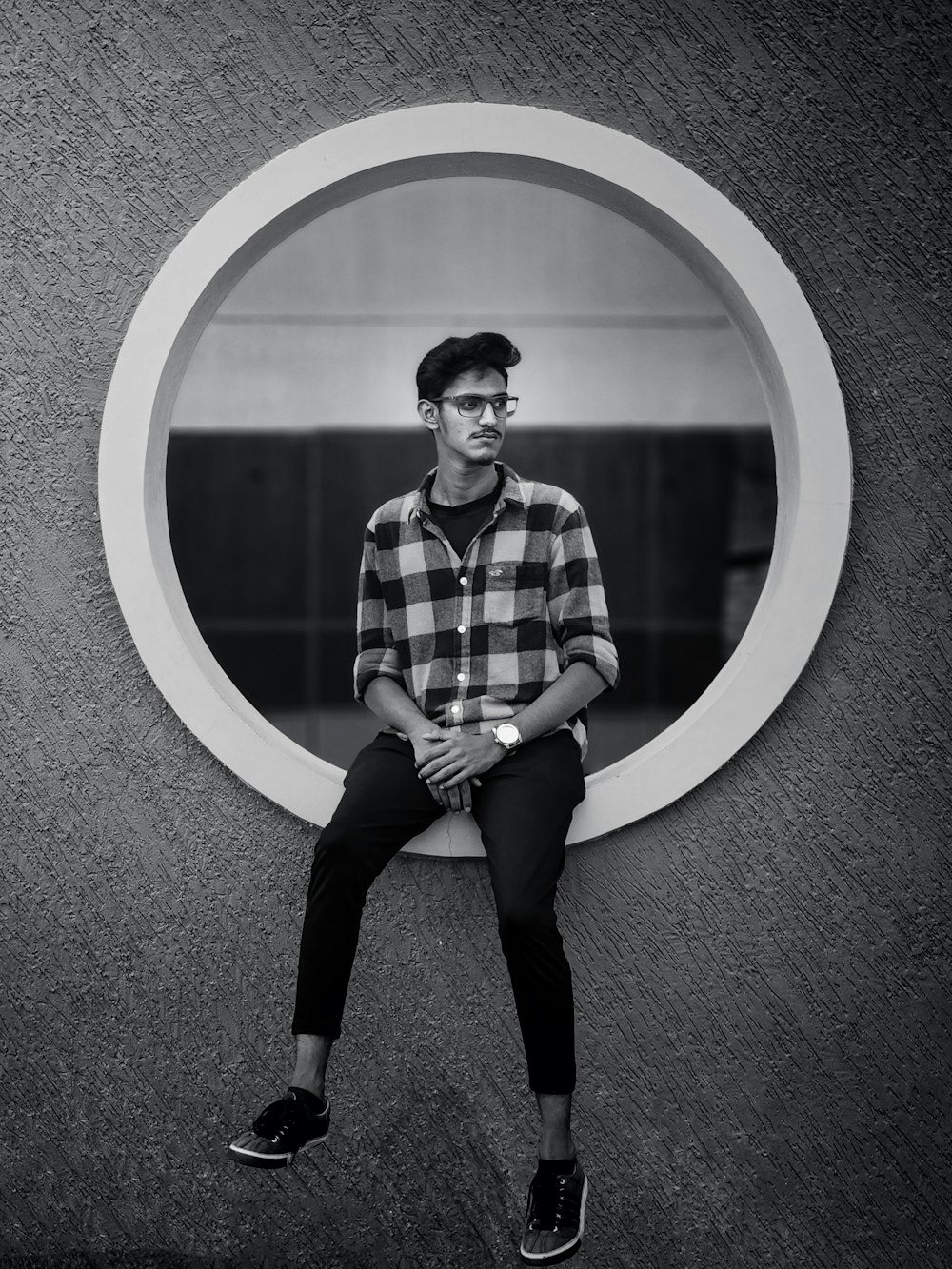 a man is sitting on a wall with a circular mirror