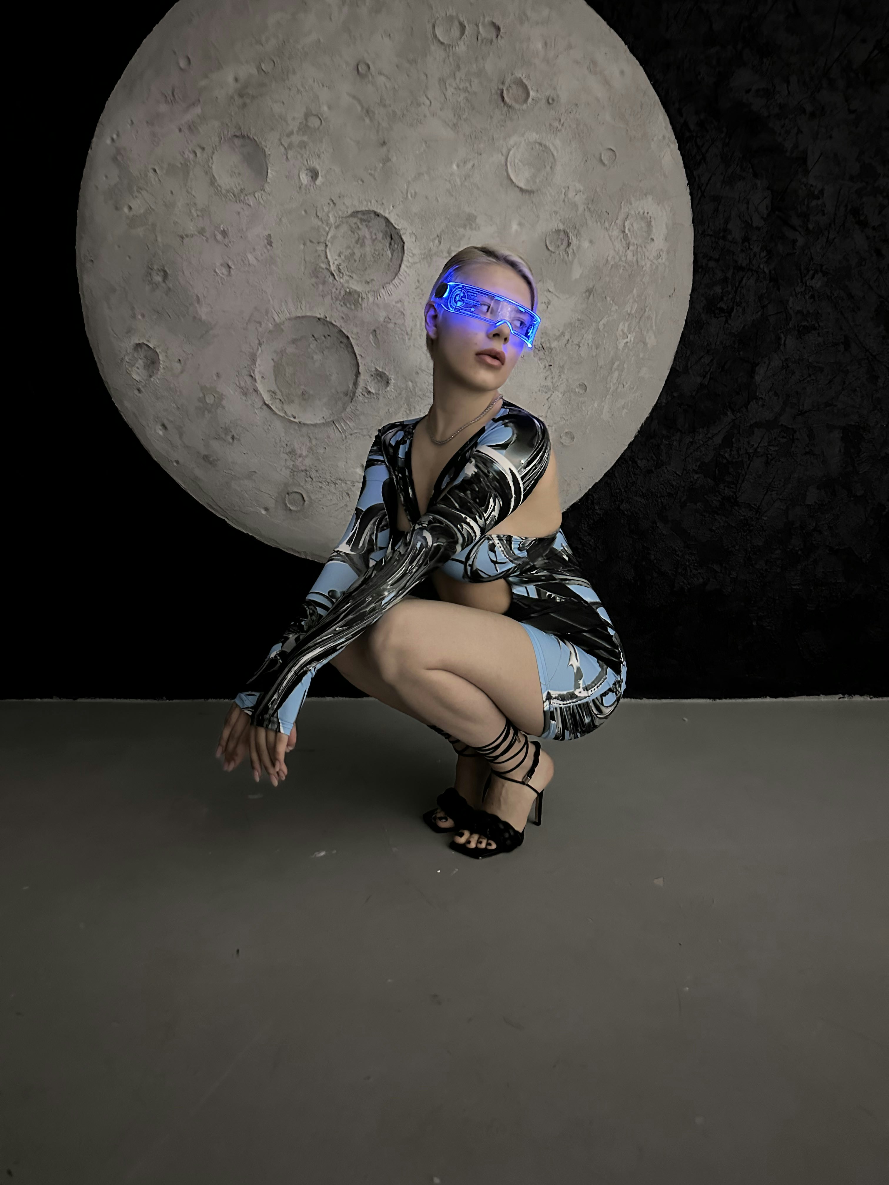 Una mujer con una luz azul en la cara arrodillada frente a una luna