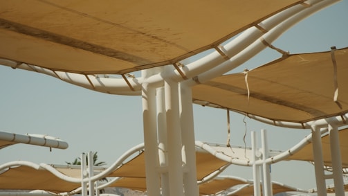A series of large, white metal structures supporting beige, canvas-like shades. The structures are closely packed and interconnected, providing shelter.