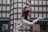 A person wearing a white outfit leaps gracefully in mid-air against a backdrop of an urban building with numerous windows. The motion captures a sense of freedom and dynamism, with the person's hair flowing and limbs extended in an elegant pose.